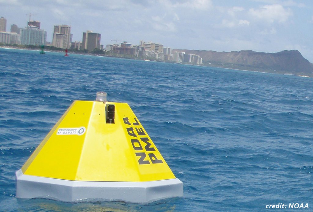A bright yellow buoy floats on blue water in the foreground with buildings and Diamond Head crater as a back drop