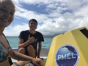 Image shows two students, grinning at the camera, with a buoy in a small boat on the water