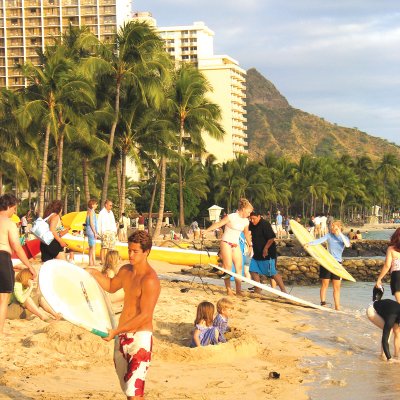 People gather on the shore of Waikiki, many have surfboards in hand