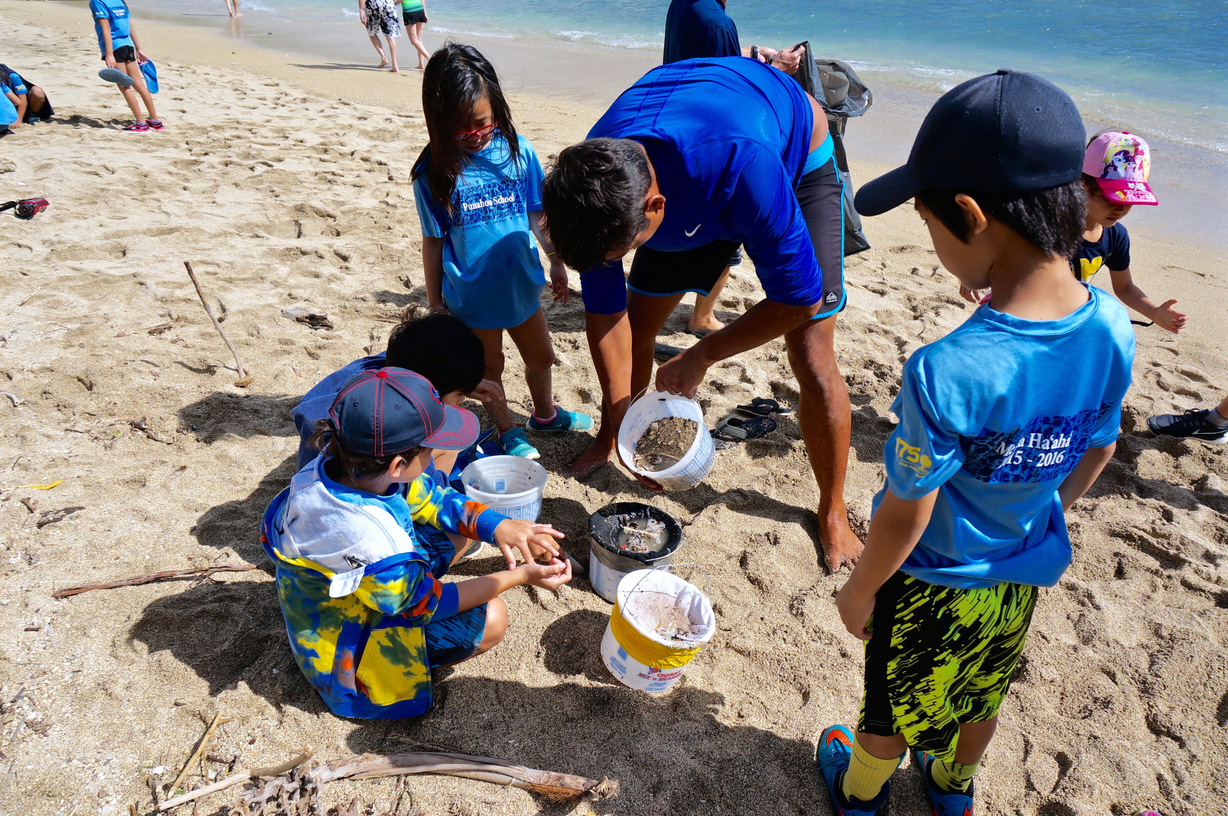 A group of young students removing microplastics cleaning beach using buckets