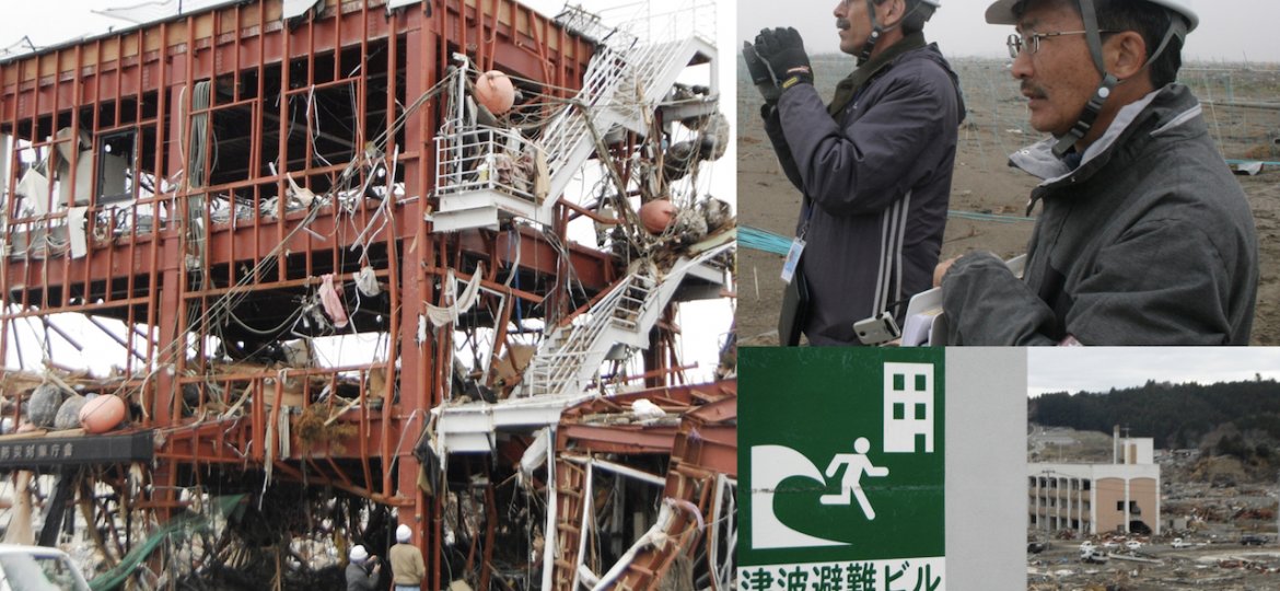 A destroyed building, two men wear hard hats and there in a sign for a 'Tsunami Evacuation Area'