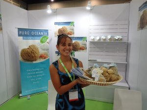 A person stands in a trade show stall, proudly holding their natural sea sponges