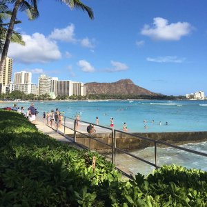A view of one part of Wakiki Beach with a walkway, beach, swimmers, buildings, and Diamond Head all in view.