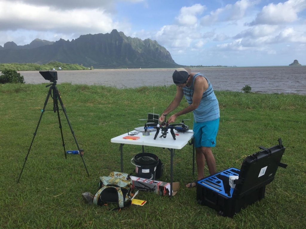 Student attaches instruments to a drone on a table in a field overlooking the bay.