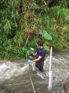 Student stands in turbulent stream taking measurements on an instrument