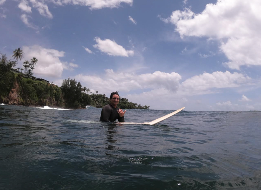 Crispin gives a shaka while sitting on his surfboard in calm waters