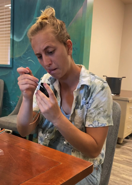 Student with a concentrated look bites on her tongue as she works on an object with a screwdriver