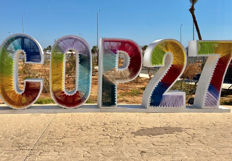 Colorful, free-standing letters and numbers spell out COP27, in a desert setting