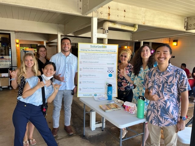 A group of seven people stand smiling around a table with an informational poster about energy