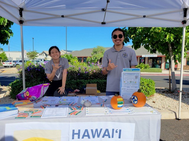 Two people throw a shaka while hosting an informational booth