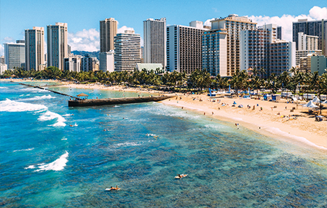 Aerial view over the ocean of waikiki beach lined with buildings.