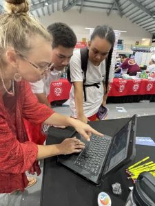 Blonde woman in red shirt leans over a computer to show two students the sea-level rise viewer on the screen