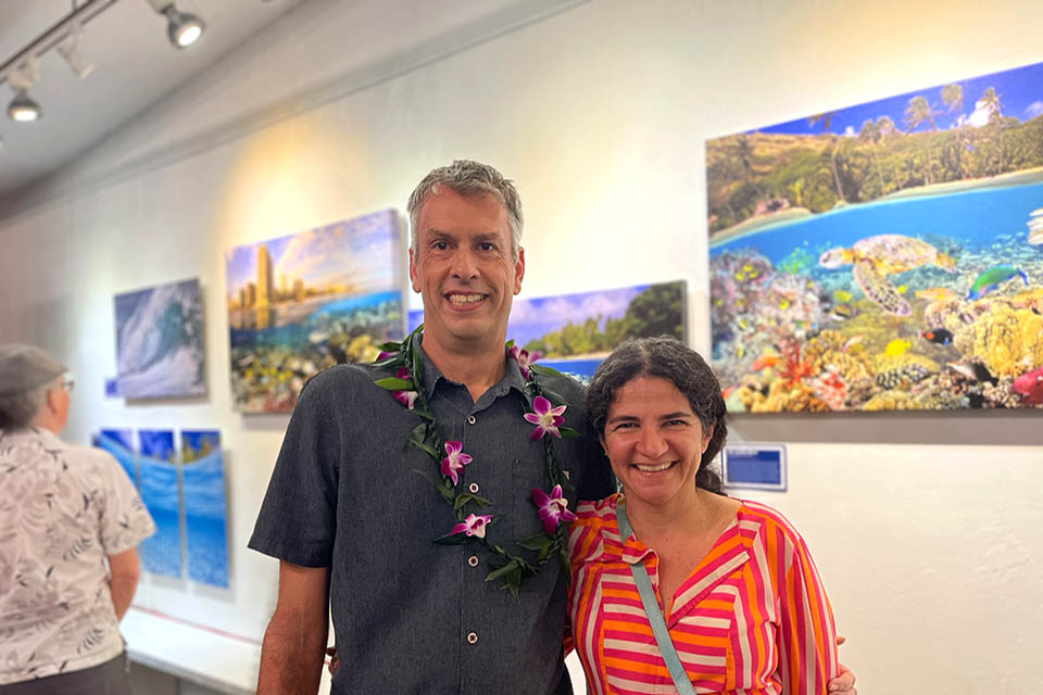 Artist and his spouse posing in front of his photographs in art gallery.