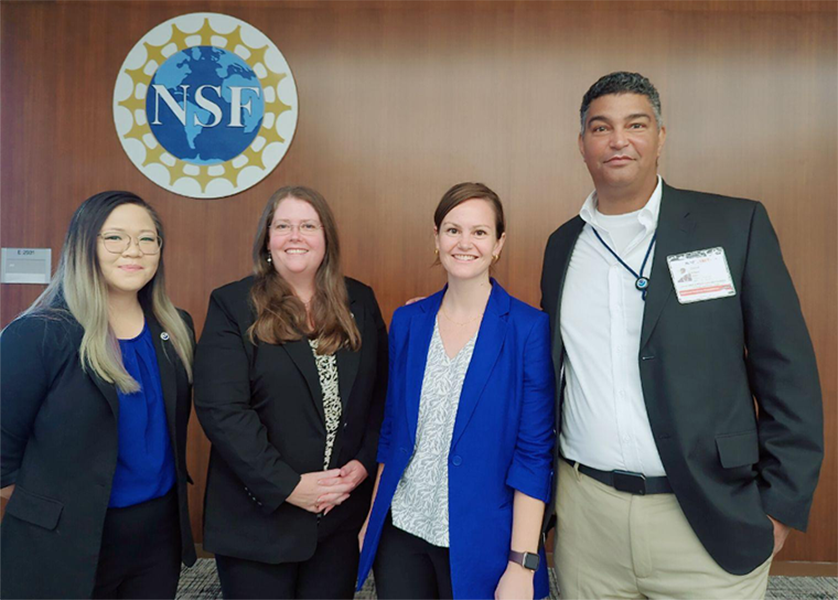 Four professionally dressed people pose below an NSF banner.