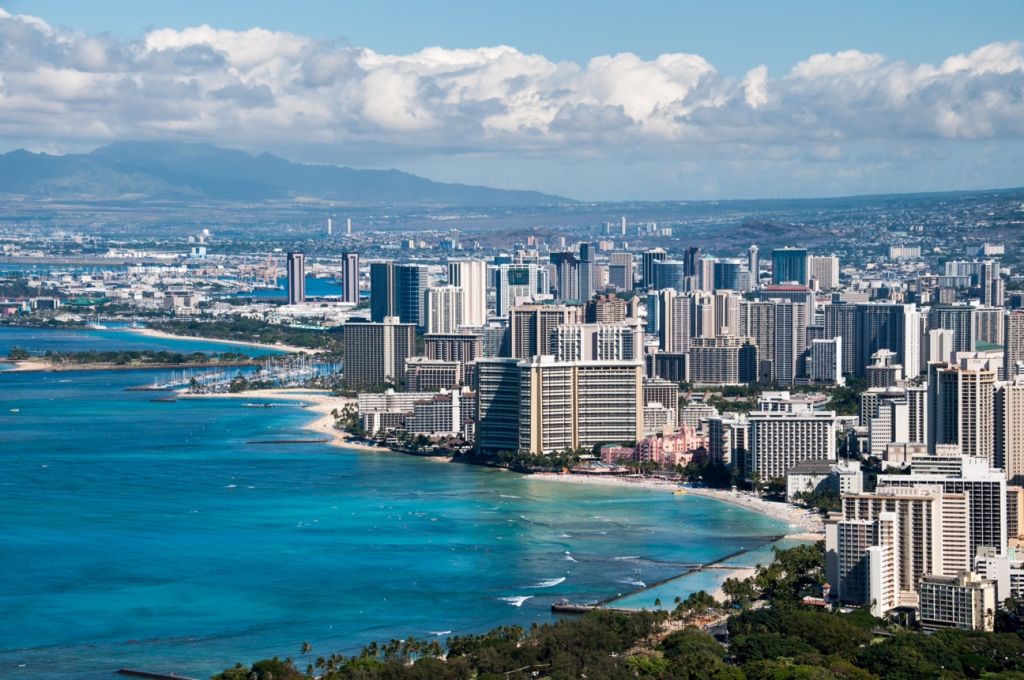 A view of the southern Oʻahu coastline, with the dense development of Waikiki in the foreground contrasting with the beautiful blue waters offshore and volcanic Waiʻanae mountains in the distance.