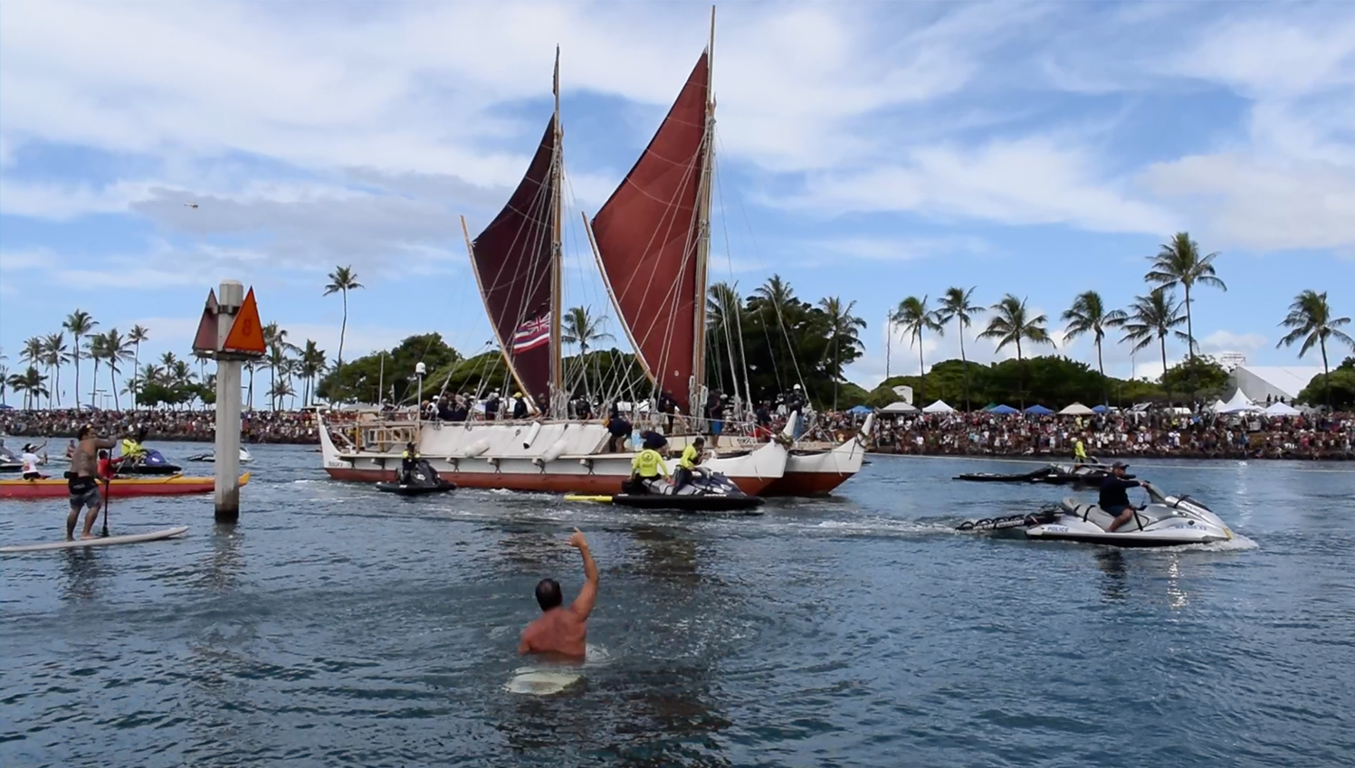Hokulea in the ocean by Magic Island, Oahu returning from a voyage. Hundreds of spectators greet the canoe on the shore.