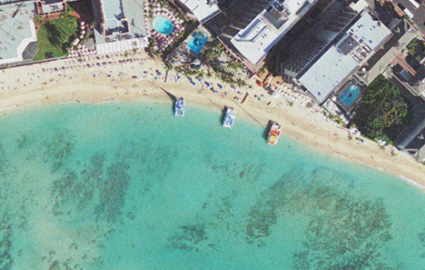 An aerial image of Waikiki beach on a sunny day, with catamarans parked on the sandy shore