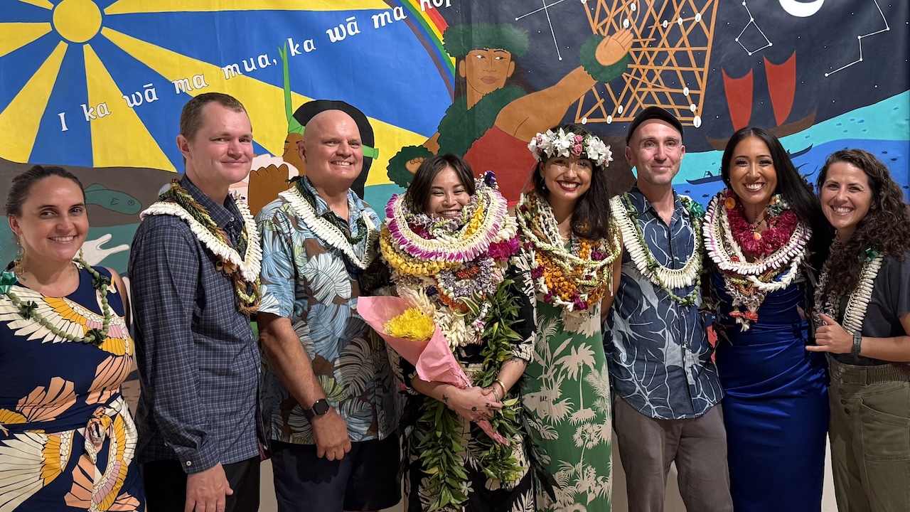 Eight people with lei on, celebrating art, in front of a large mural